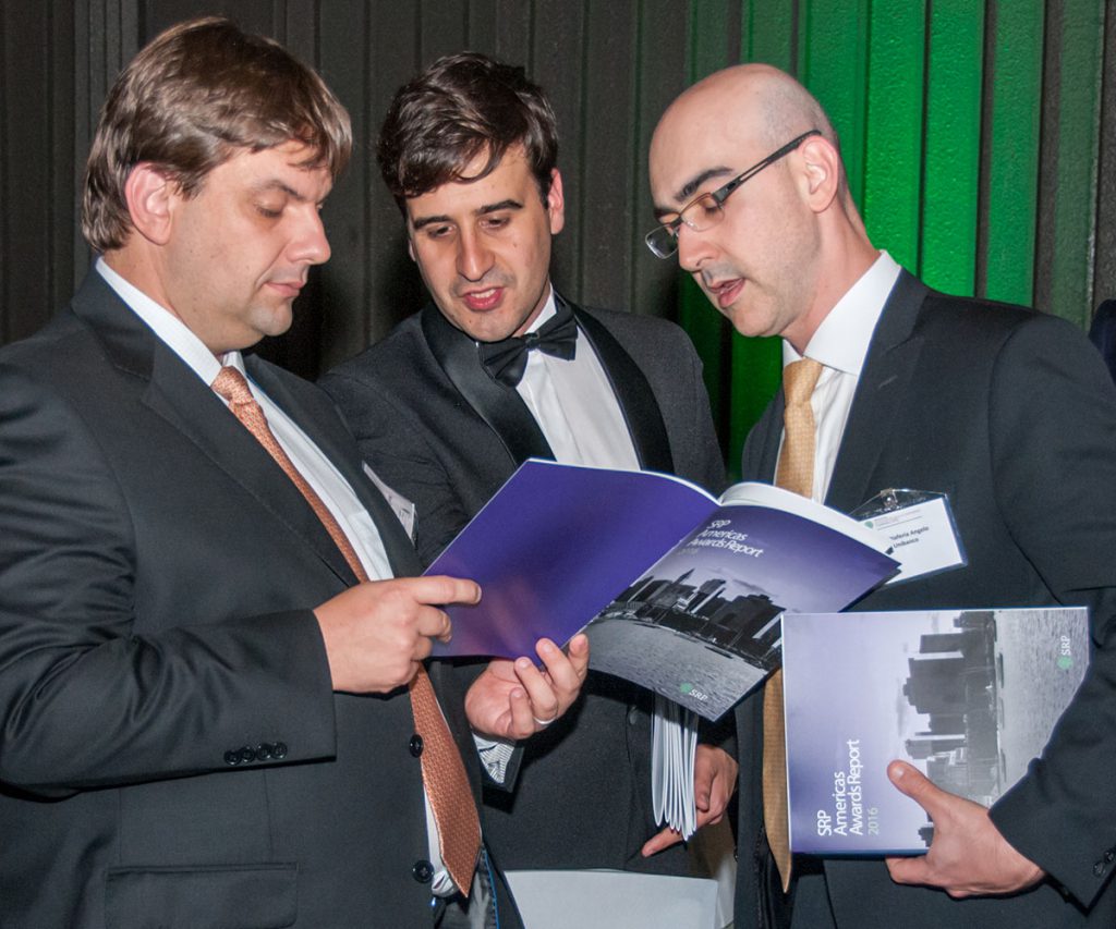three men examine the program at an awards event