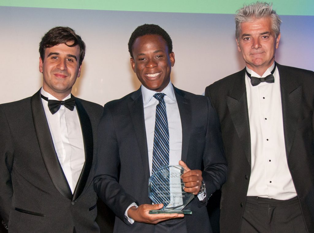 young man smiles and holds the award he just received